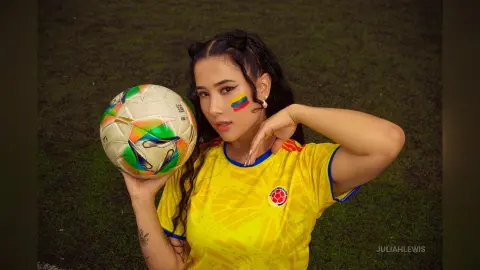 JuliahLewis poses in a yellow soccer jersey while holding a soccer ball against a green grass background.