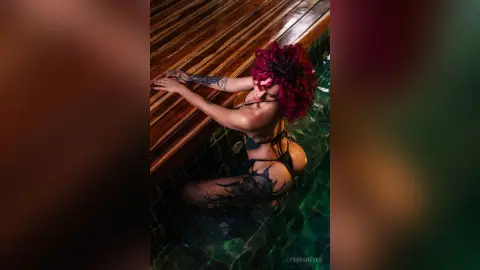 Tattooed woman in black bikini relaxing in a luxury pool at night with a moody, cinematic atmosphere.