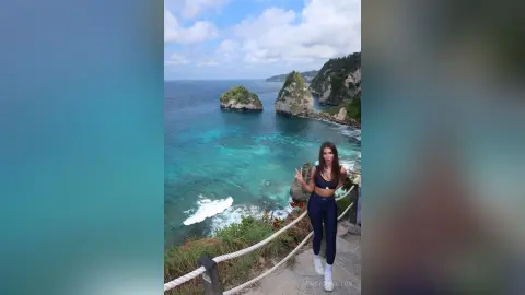 Young woman in navy blue activewear standing on a coastal cliff overlooking turquoise ocean waves.