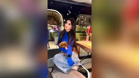 JuliDeming sits outside at night wearing a blue long-sleeve shirt and light jeans while holding a small brown dog.