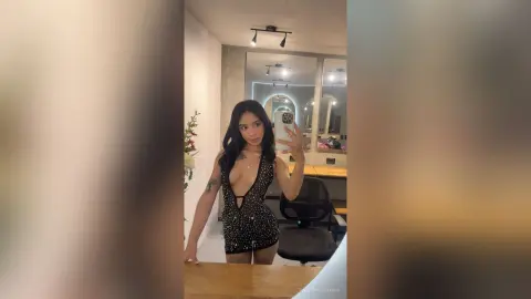 Glamorous woman in a black sequined plunging bodysuit taking a selfie in a modern dressing room.