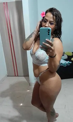 Curvy woman in white lace lingerie taking a mirror selfie in a bright bedroom.