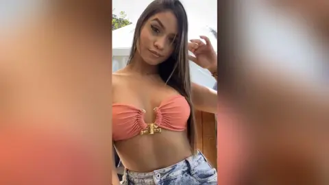 Young woman in a peach bandeau bikini top posing outdoors in bright sunlight.