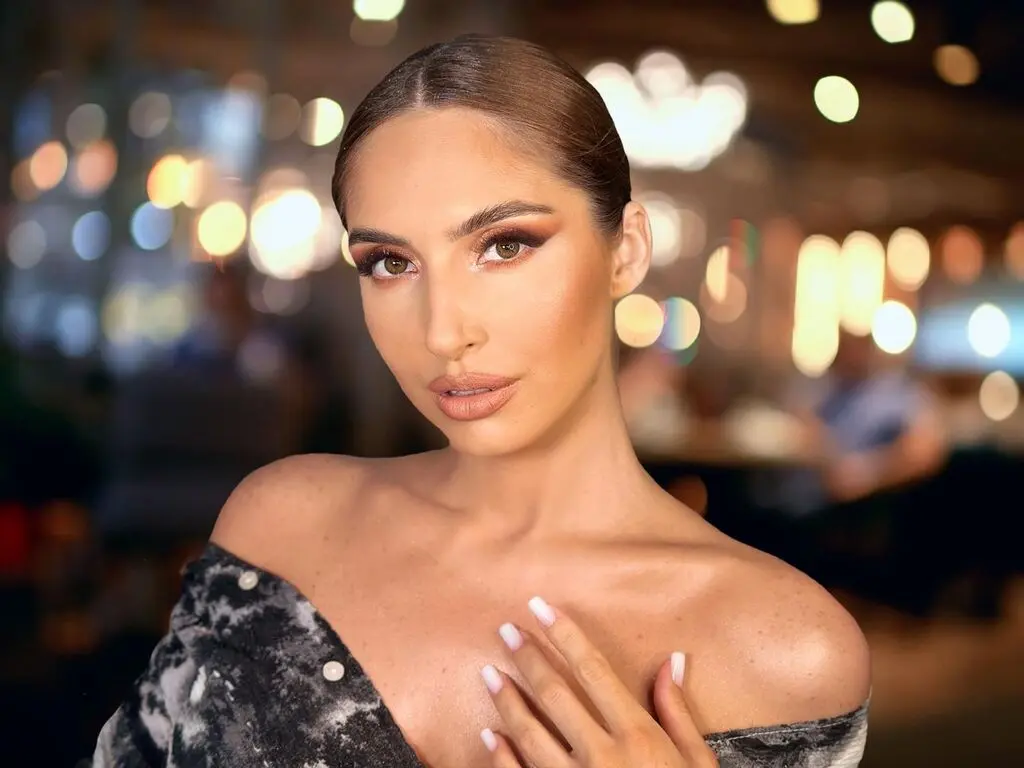 Glamorous woman with elegant updos and glowing makeup posing in a warm, bokeh-lit restaurant setting.