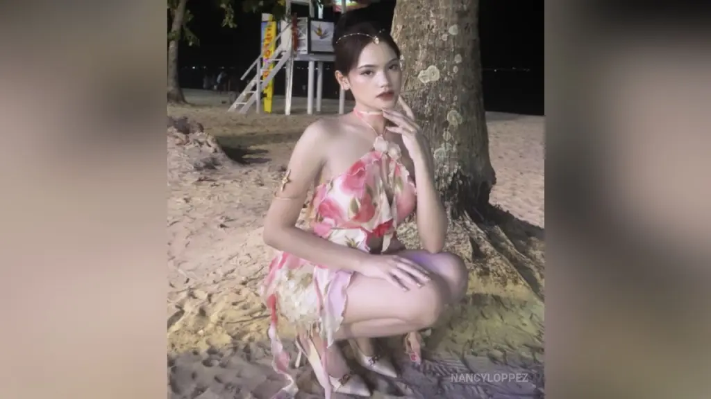 NancyLoppez โ Elegant woman in a pink floral sundress posing on a sandy beach at night under moonlight.