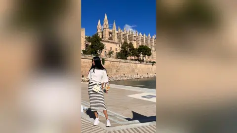 LucyMartin stands on a stone walkway in a white top and black and white striped skirt, with a large cathedral in the background.