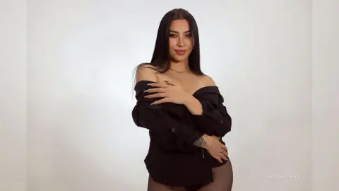 Smiling woman in an elegant black off-the-shoulder blouse posing against a clean white studio background.