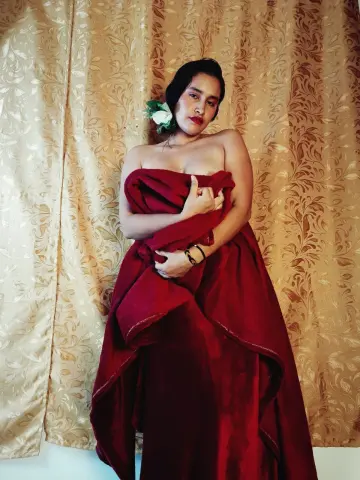 Elegant woman in a flowing red velvet wrap dress posing against a gold patterned backdrop.
