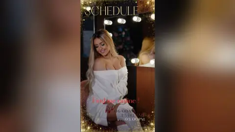 Anita poses in a white off-the-shoulder top, showing cleavage, while looking down with her blonde hair falling over her shoulder.