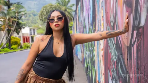 ChloeRiveiro — Stylish woman in a black halter top and sunglasses posing by a colorful street art mural in a sunny outdoor setting.