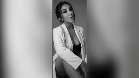 Elegant woman in a white blazer and black top posing for a sophisticated black and white portrait.