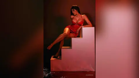 Elegant woman in a red satin slip dress sitting on white stairs in moody, cinematic lighting.