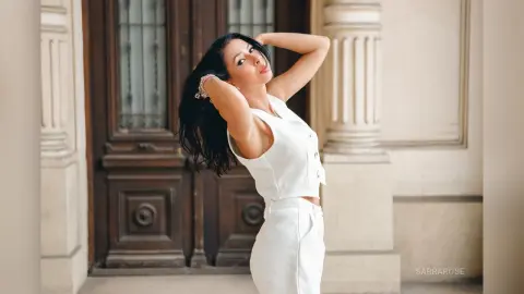 Elegant woman in a white sleeveless outfit posing confidently in front of a classic vintage wooden door.