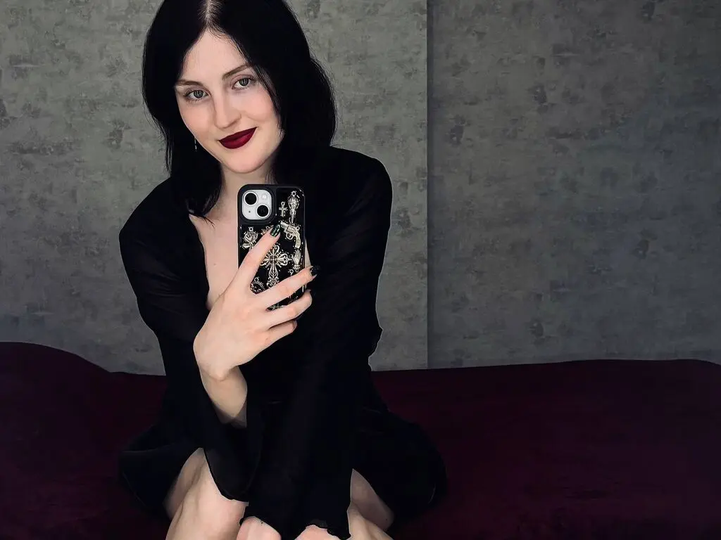 Woman with dark hair and red lipstick wearing a black outfit taking a moody mirror selfie indoors.