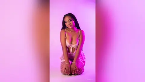 Young woman in white lace lingerie posing against a soft pink studio background with a dreamy mood.