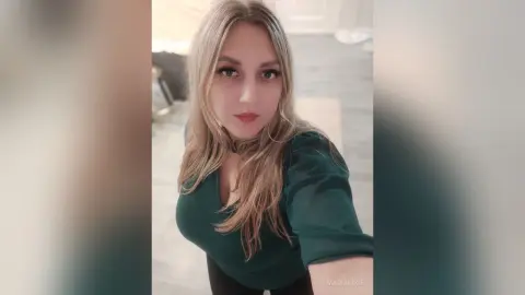MariaPixie poses in a dark green long-sleeved top with her long blonde hair styled down.