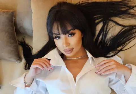 Young woman with long dark hair in a white button-down shirt relaxing on a beige sofa with a serene mood.