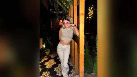 SofiaRoose poses outdoors at night wearing a tan crop top and white pants, showing her midriff and blonde hair.