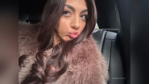 Young woman with long wavy hair wearing a cozy pink faux fur coat sitting in a car.