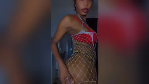 AngelaGoodwin poses in a red bra and white fishnet bodysuit, showing off her slim figure and dark hair against a simple indoor background.