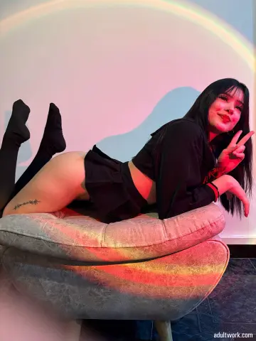 Young woman in black outfit lounging on a plush chair under warm, colorful lighting.