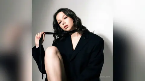 Elegant woman in a black blazer and necktie posing against a minimalist white background with a moody aesthetic.