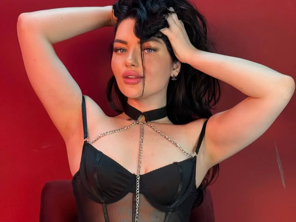 Beautiful woman in black lace lingerie and choker posing against a red background with a moody expression.