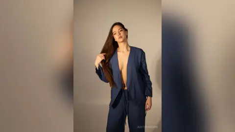 Elegant woman in a navy blue silk pajama set posing against a neutral studio background with a moody aesthetic.