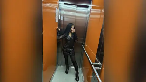 AlmaKane — Stylish woman in a black leather outfit taking a mirror selfie in a modern elevator.