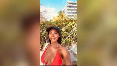 Smiling woman in a red bikini and black cap enjoying a sunny tropical vacation day outdoors.