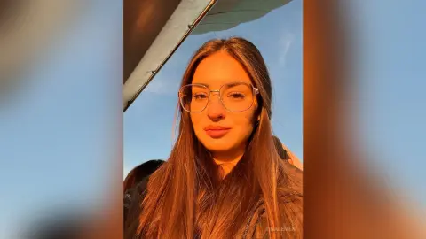 Smiling young woman with long brown hair and glasses outdoors during a warm golden hour sunset.