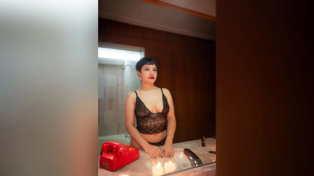 Woman in black lace lingerie and stockings lying on a wooden floor in a moody, intimate indoor setting.