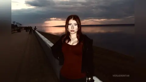 Young woman in a dark jacket and red top standing by a lake at sunset with a moody, cinematic atmosphere.