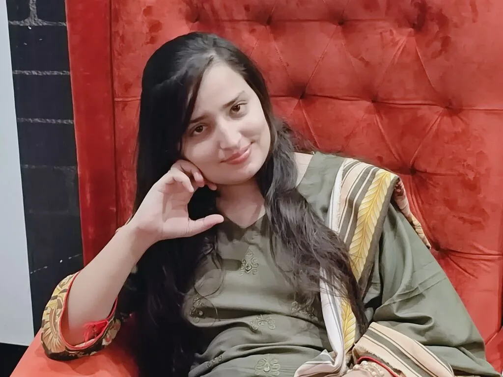 AyeshaSajid — AyeshaSajid wears a black patterned headscarf and top while sitting by a riverbank.