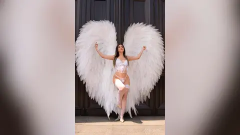 Ethereal woman in white lace lingerie wearing massive white angel wings against a dark door background.