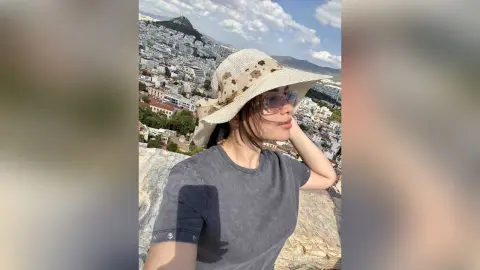 Young woman in a grey t-shirt and straw sun hat enjoying a sunny view over a Mediterranean coastal city.