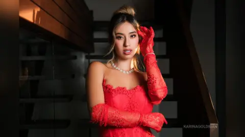 Elegant woman in a red lace evening gown and matching gloves posing glamorously on a dark staircase.