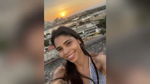 Smiling young woman in a blue striped top enjoying a sunset view over a coastal city skyline.