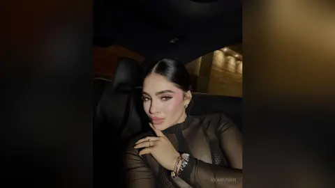 Young woman in a black sheer top posing inside a car with moody, low-light evening lighting.