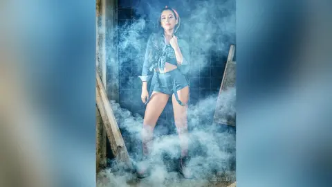 JessieLiu stands upright in denim shorts and a matching denim top, surrounded by thick white smoke or steam.