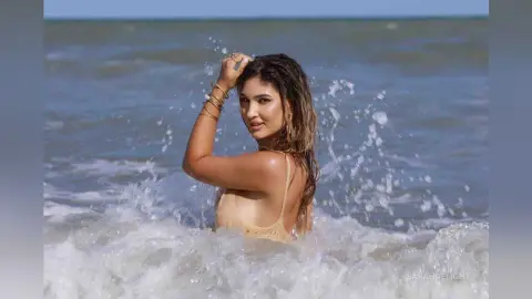 Beautiful woman in a beige bikini relaxing in ocean waves at a sunny beach.