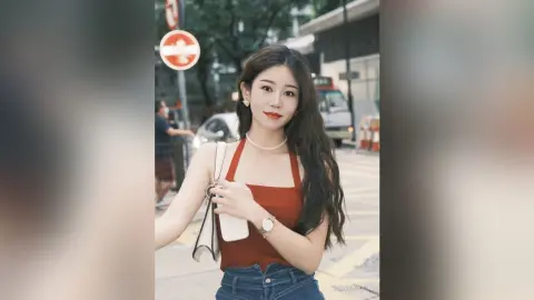Smiling young woman in a red tank top and jeans posing on a city street during the day.