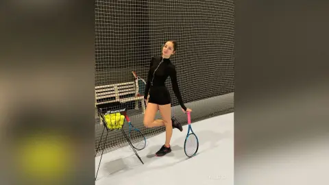 Athletic woman in black tennis outfit holding a racket on an indoor court with a confident mood.