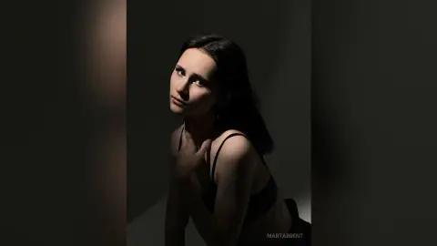Moody portrait of a young woman in black lingerie against a dark, dramatic studio background.