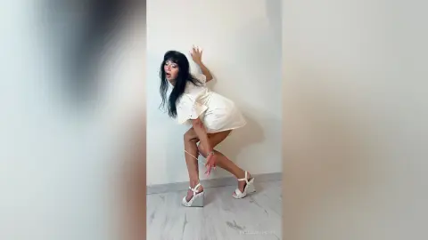 Cheerful woman in a white lace dress and platform sandals dancing in a bright minimalist room.