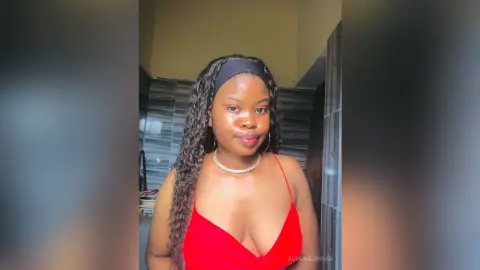 Smiling young woman in a red tank top and pearl necklace posing in a modern bathroom setting.