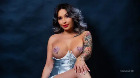 Glamorous woman in a silver metallic corset with heart-shaped pasties posing against a dark studio background.