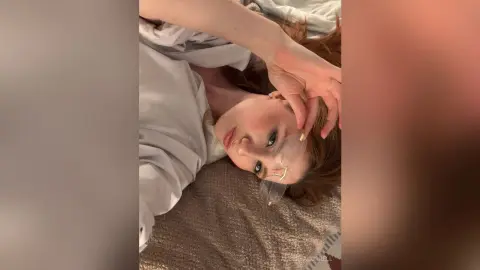 AlbertaCorrell lies on a brown blanket wearing a white shirt and looking at the camera.