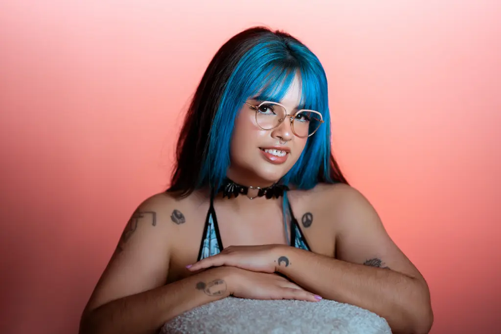 MaddieWaves shows off her light blue hair and face, wearing a black and white striped top while looking directly at the camera.