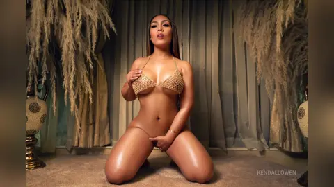Glamorous woman in a gold sequin bikini posing in a luxurious room with elegant drapery and pampas grass decor.